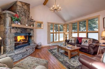 A cozy living room with a stone fireplace and large windows overlooking a snowy scene outside.