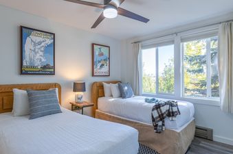 A bright and airy bedroom in Gros Ventre A10 featuring two twin beds, vintage posters, and large windows with scenic outdoor views.