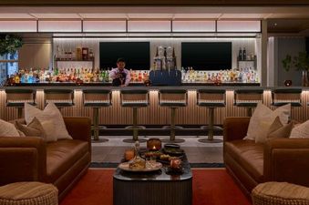 A modern bar with dark wood and leather seating, as well as a bar counter with a bartender serving drinks.