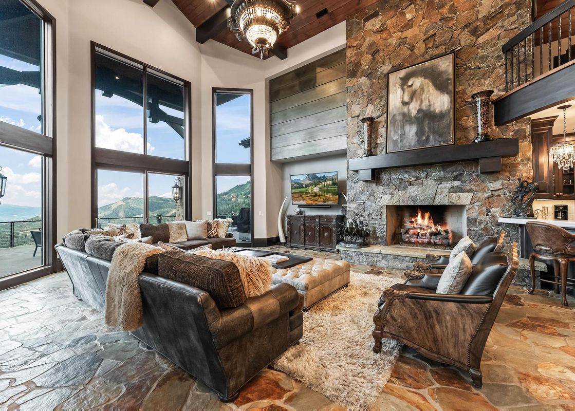 A luxurious rustic living room with a large stone fireplace, plush seating, and floor-to-ceiling windows offering mountain views.