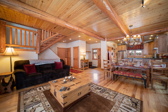 A spacious living area with exposed wooden beams, a comfortable sofa, a rustic coffee table, and a dining area leading to a well-appointed kitchen.