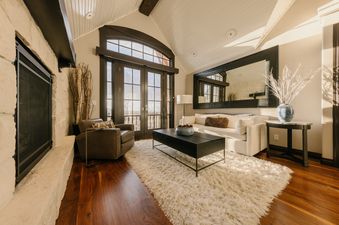 The living area of Red Hawk Retreat at See Forever features a white sofa, a brown armchair, a fireplace, and large glass doors leading to an outdoor view.
