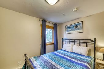 A bedroom with a bed with a blue and green comforter, a window with curtains, and a framed picture of penguins on the wall.