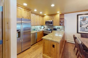The kitchen at Manor Vail 115 has stainless steel appliances, wooden cabinets, granite countertops, and a breakfast bar.