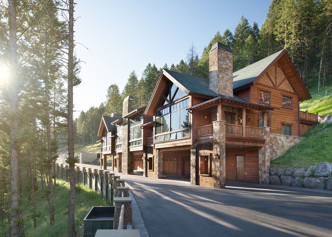Exterior view of The Nest in Jackson Hole featuring rustic wooden lodges surrounded by pine trees under a clear sky.