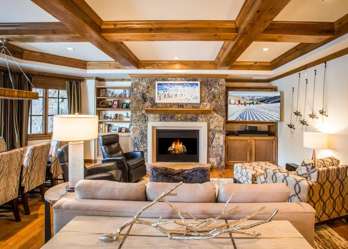 An elegant and warm living room in Chateau Beaver Creek Residence 1304, featuring a stone fireplace, large TV, comfortable sofas, and wooden accents, creating a cozy and luxurious atmosphere.