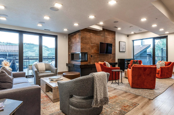 A modern and cozy living area at Kings Crown Hideaway features a striking fireplace, comfortable sofas and armchairs, and large windows with scenic views.