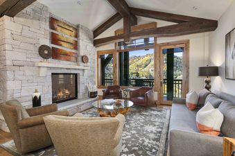 A wide shot of the grand living area in Silver Strike Lodge 703, featuring a stone-faced fireplace, plush seating, and expansive windows with mountain views.