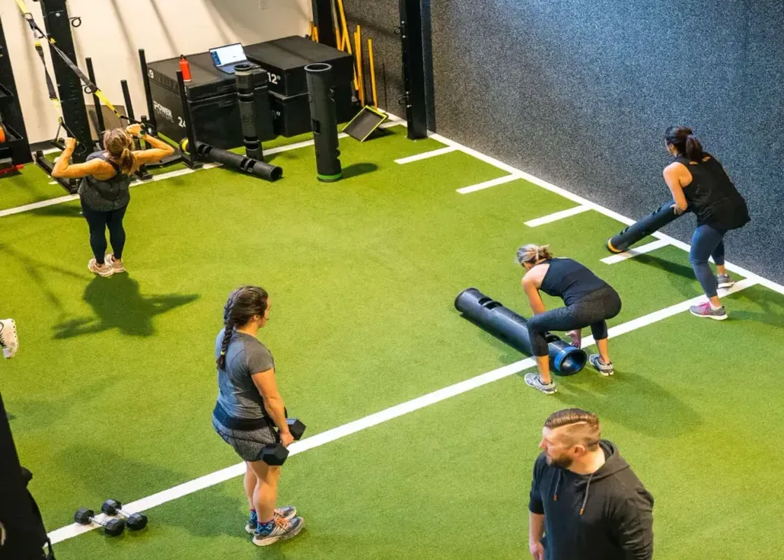 A high-angle view of the turf gym area at Gravity Haus JH ADA Two Queen and Roll In during a workout session with multiple people.