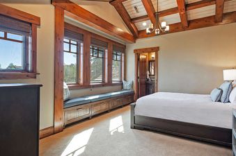 A spacious bedroom features a large window seat with gray cushions and multiple windows, providing a bright and inviting atmosphere, perfect for relaxation.