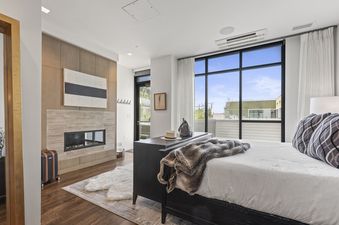 A modern master bedroom at Parkite 37 featuring a king-sized bed, a fireplace, and large windows with urban views.