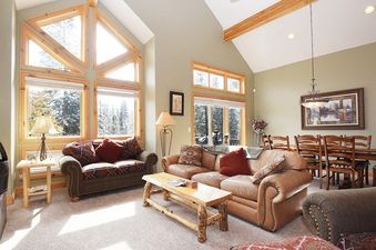 A spacious and inviting living area and dining room within Timberlake 341, featuring comfortable sofas, a rustic coffee table, a dining set, and large windows with outdoor views.