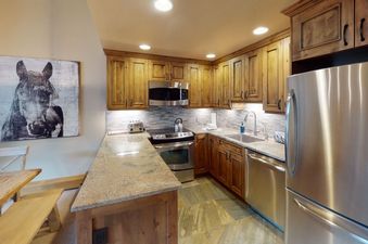 The kitchen in Manor Vail 218 features stainless steel appliances, a breakfast bar, and wooden cabinetry.