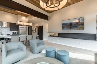 A modern open-plan living and kitchen area with light blue armchairs, a linear fireplace, and a large TV.