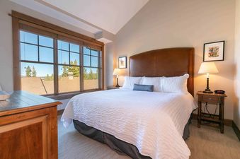 A bedroom with a white duvet, a leather headboard, and a window overlooking the mountains.