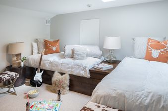 A cozy double twin bedroom in Pines Garden 4140 with rustic decor, featuring two beds with white bedding and decorative pillows, a guitar, and a board game set up on the floor.