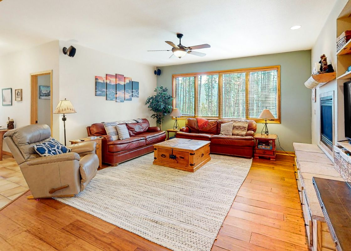 The living room at Big Moose Lodge features leather couches, a wooden coffee table, and a view of the forest.