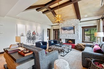 A spacious and elegantly decorated living room with a vaulted ceiling, a stone fireplace, comfortable seating, and large windows offering a view of the outdoors.