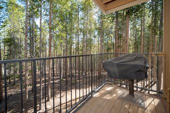 The balcony at Beaver Village 1624 offers a tranquil escape, featuring a grill for outdoor cooking and surrounded by the serene beauty of a lush pine forest.