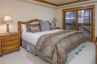The bedroom in Vail Mountain View 402 features a king-size bed with a decorative headboard and a patterned comforter, along with a nightstand and lamp.