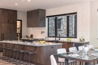 A modern kitchen and dining area in Triple 3 Lodge feature dark wood cabinetry, a large kitchen island with bar stools, and a glass dining table.
