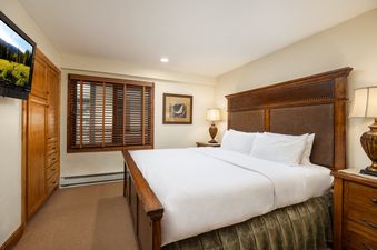 A cozy bedroom at Montaneros 420 with a large bed, wooden furniture, and a wall-mounted TV.