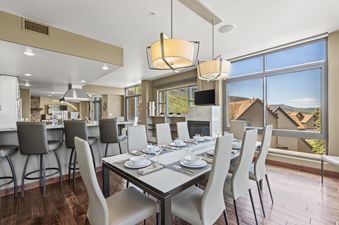 A wide view of the modern dining room and kitchen in Lowell 401 0, featuring a dining table set for eight, contemporary pendant lighting, and large windows with mountain views.
