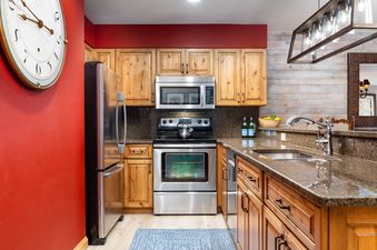 A modern kitchen with wood cabinets, stainless steel appliances, and red walls.