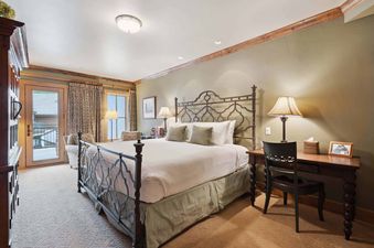 A large bedroom with a bed with an ornate metal headboard, a desk, and a door leading to a balcony.