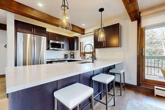 A modern kitchen with stainless steel appliances, dark wood cabinets, and a white quartz countertop with bar stools at Slope 101.