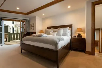 A luxurious master bedroom with a king-sized bed, dark wood furniture, and a private balcony overlooking a snowy village scene.