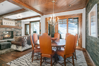The dining room at Grand Lodge 3 Bedroom Deluxe 304 features a round table with six chairs, a fireplace, and a large window with views of a ski slope.