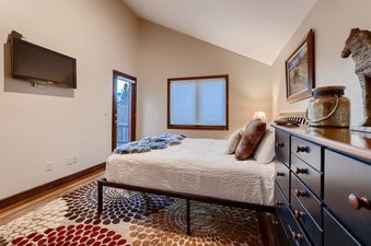 A cozy bedroom at Ullr Haus with a comfortable bed, a TV mounted on the wall, and a door leading to a balcony with mountain views.