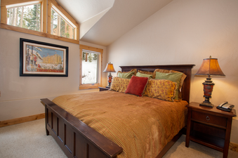 A cozy bedroom with a large bed, two bedside tables with lamps, and windows offering a view of snowy trees.