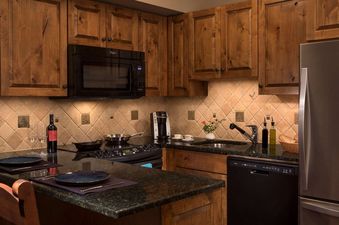 A well-equipped kitchenette with warm wood cabinets, dark granite countertops, and modern appliances.