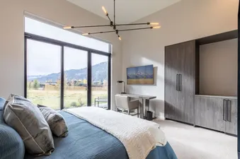 A modern bedroom with a large bed, floor-to-ceiling windows offering mountain views, and sleek dark wood furniture.