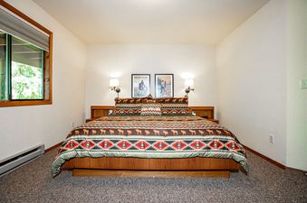A cozy bedroom in The Cedar Nest with a large bed featuring a patterned comforter, rustic artwork, and a window overlooking greenery.