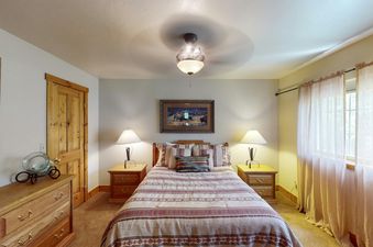 A bedroom at Bear Creek Lodge Townhome features a comfortable bed with a southwestern-themed duvet, two nightstands with lamps, and a large window with sheer curtains.