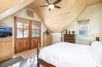 A bedroom with a large bed, a wooden dresser, and a ceiling fan. There are french doors leading to a balcony.