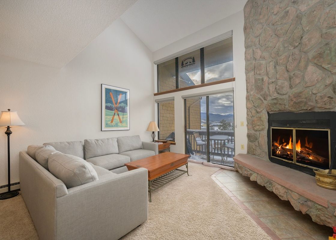 The living room at Meadow Ridge 31 features a large sectional sofa, a coffee table, a fireplace, and large windows with a snowy mountain view.