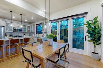 A modern dining room and kitchen with a wooden dining table, contemporary chairs, and a kitchen island with bar stools.