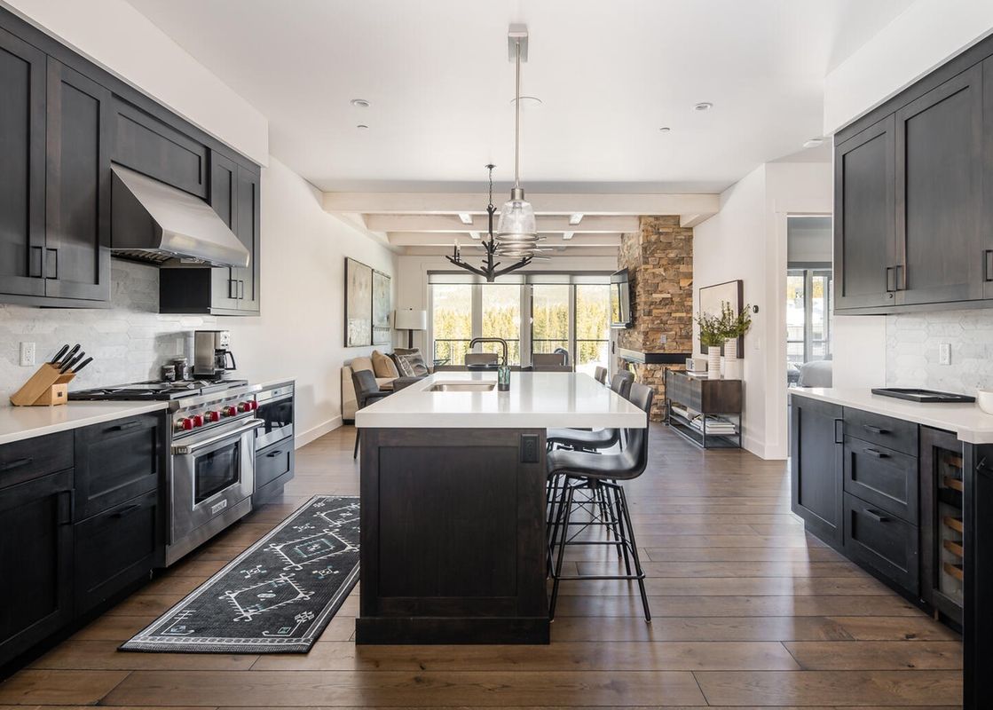 The modern kitchen at Moonlight Basin 16 Wildwood features stainless steel appliances, dark cabinetry, a center island with seating, and a large, bright window.