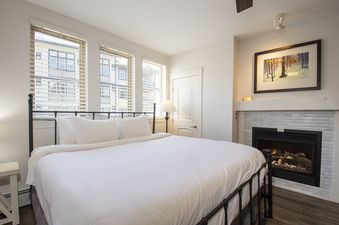 A cozy bedroom at Fraser Crossing Studio 3518 with a bed, fireplace, and windows with blinds.