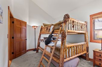 A rustic bunk room at Crescent Cabin with a wooden bunk bed, leopard print bedding, a unique floor lamp, and a wooden door.
