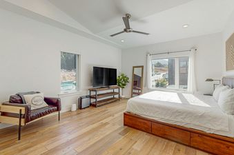 The bedroom at Sandlewood Sanctuary features a king-size bed with white linens, a large window with a view of the mountains, a flat-screen TV, and a comfortable chair.