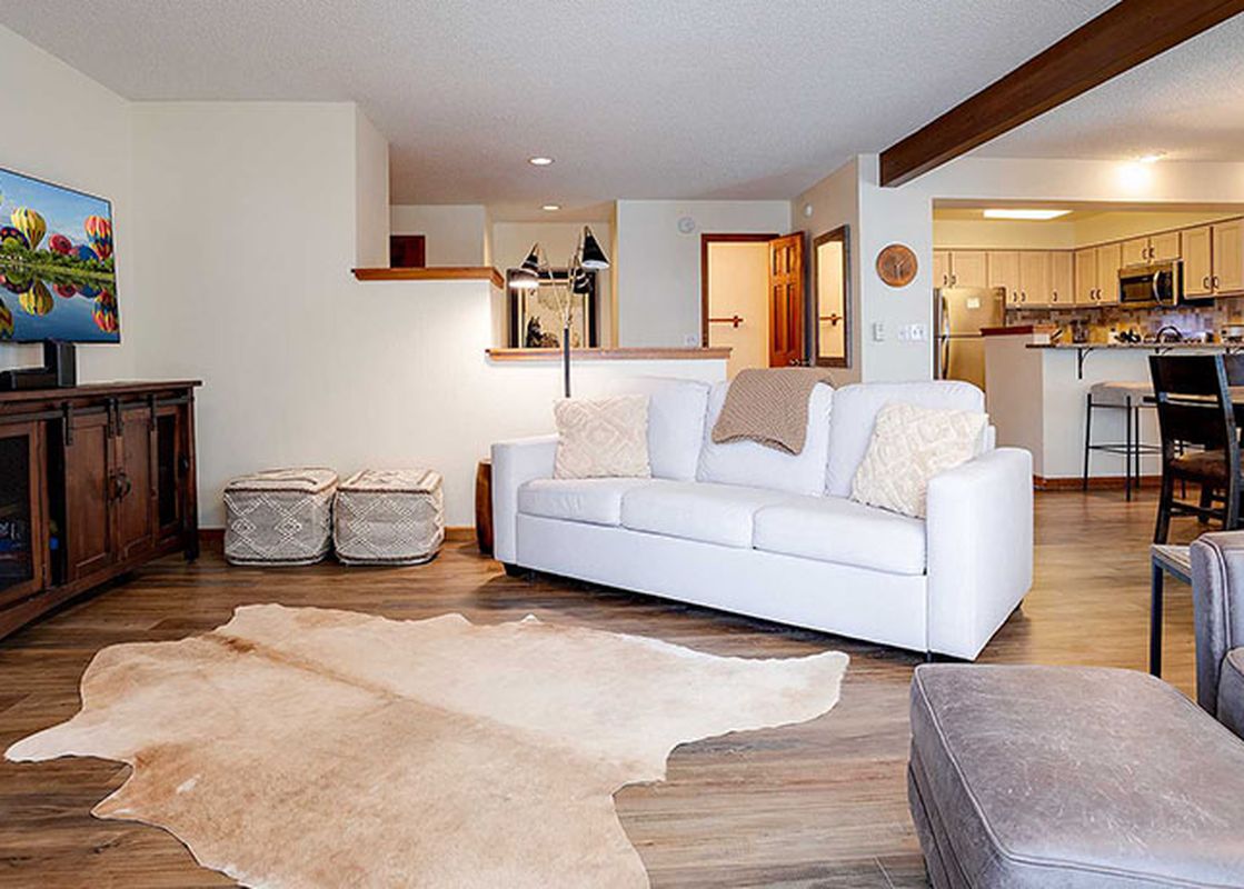 A wide view of the open-concept living room, kitchen, and dining area at Ranch at Steamboat RA203, featuring a white sofa, a large TV, a hide rug, and a modern kitchen.