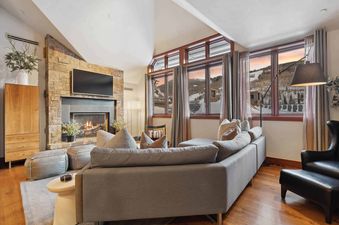 A living room with a sectional sofa, a fireplace, and a large window with a view of the mountains.