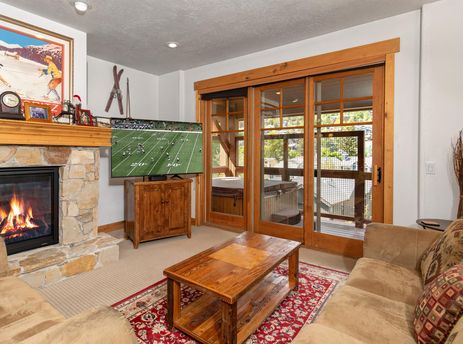 A cozy living room in Town Pointe C302 with a lit fireplace, a flat-screen TV showing a football game, comfortable sofas, and access to a patio with a hot tub.