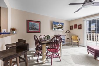A cozy dining area features a wooden table with red chairs, a wall-mounted TV showing a ski resort, and a breakfast bar with wooden stools.