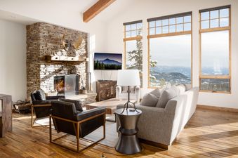A luxurious living room with a stone fireplace, smart TV, comfortable seating, and large windows revealing a stunning snowy mountain landscape.